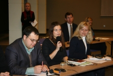 Uczestnicy seminarium siedzą w ławkach. Jedna osoba zabiera głos przez mikrofon.