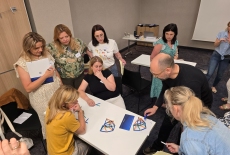 Uczestnicy siedzą przy stole i układają patyczki.