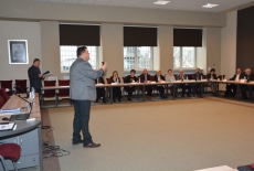 Uczestnicy Akademii siedzą przy stolach, a na środku stoi przemawiający Pan