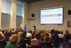 Prelegent przemawia przy mównicy, na sali siedzi widownia