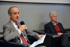 Ambasador Janusz Reiter przemawia siedząc w prezydium. Obok Niego siedzi prof. Roman Kuźniar.