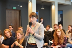 Uczestnicy spotkania siedzą w Auli KSAP. Pani zadaje pytanie przez mikrofon.