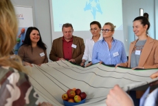 uczestnicy trzymają materiał, na którym stoi miska z jabłkami