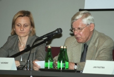 Dwoje prelegentów siedzi przy stole. Pan mówi do mikrofonu.