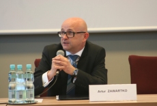 Artur Zawartko siedząc przy stole przemawia do mikrofonu.