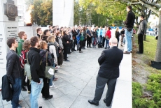 Słuchacze stoją przy pomniku.