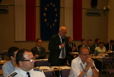 Zgromadzeni uczestnicy konferencji siedzą na auli, jeden z uczestniczów mówi do mikrofonu