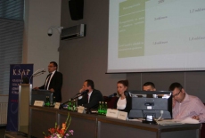 Pan stoi na mównicy i przemawia siedzą prowadzący  konferecję