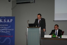 Pan stoi na mównicy i przemawia siedzą prowadzący  konferecję