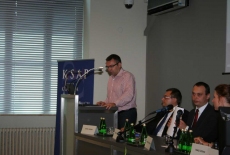 Pan stoi na mównicy i przemawia siedzą prowadzący  konferecję