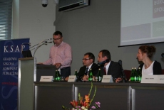 Pan stoi na mównicy i przemawia siedzą prowadzący  konferecję