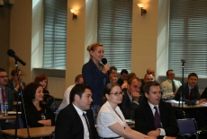 Zgromadzeni uczestnicy konferencji siedzą na auli, jedna z uczestniczek mówi do mikrofonu