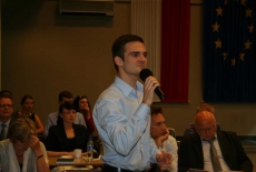 Zgromadzeni uczestnicy konferencji siedzą na auli, jeden z uczestniczów mówi do mikrofonu