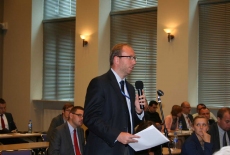 Zgromadzeni uczestnicy konferencji siedzą na auli, jeden z uczestniczów mówi do mikrofonu