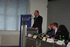 Pan stoi na mównicy i przemawia siedzą prowadzący  konferecję