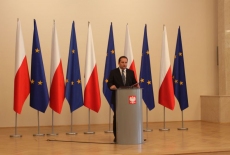 fot. Sebastian Szulfer/KSAP Tomasz Arabski stoi przy mównicy i przemawia na tle flag Polski i UE