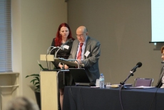 fot. Sebastian Szulfer/KSAP Pan stoi i przemawia przy mównicy. obok stoi Pani w czerwonych włosach