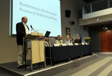 Pan stoi na mównicy i przemawia  za nim wyświetlana jest prezentacja