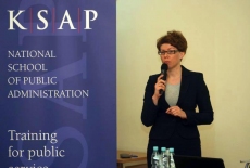 Katarzyna Woś mówi do miktofonu stojąc pod rollup KSAP.