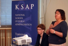 Katarzyna Woś siedzi w prezydium, a Pani Klaudia Torres-Bartyzel stoi i przemawia przez mikrofon.