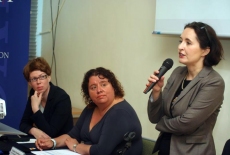 Katarzyna Woś i Pani Klaudia Torres-Bartyzel siedzą w prezydium, a trzecia Pani stoi i przemawia przez mikrofon.