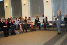 Jedna z osób siedzących na sali zadaje pytanie prowadzącej dyskusję. Uczestnicy siedzą w półkole, a prelelegentka stoi pośrodku.