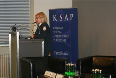 Uczestniczka sesji warsztatowej mówi do mikrofonu stojąc przy mównicy.