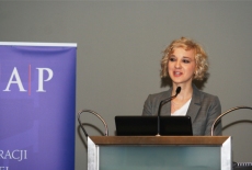 Uczestniczka sesji warsztatowej mówi do mikrofonu stojąc przy mównicy.