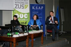 Uczestnicy sesji warsztatowej siedzą w prezydium. Jedna osoba mówi przez mikrofon.