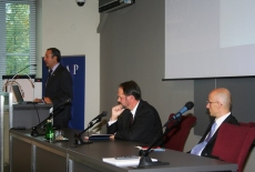  Ambasadorem Felipe Gajardo przemawia przy mównicy, a prozostali prelegenci siedzą przy stole.