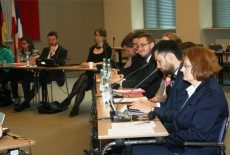 Grupa uczestników konferencji siedzi przy ławkach. 