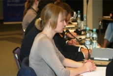 Uczestniczka siedząc za stołem zadaje pytanie do mikrofonu.