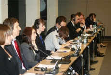 Uczestnicy siedzą przy stole zasłuchani, korzystają ze słuchawek, jedna osoba robi notatki.