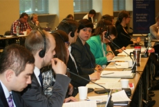 Uczestnicy siedzą przy stole zasłuchani, korzystają ze słuchawek.