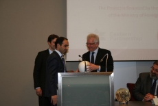 Dyrektor KSAP Jacek Czaputowicz stoi przy mównicy i wręcza upominek uczestnikom