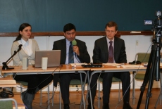 Troje prowadzących siedzi przy ławkach jeden z nim trzyma mikrofon i mówi