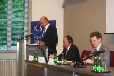 Francuski Sekretarz Stanu Harlem Désir przemawia stojąc przy mównicy. Obok niego za stołem prezydialnym siedzą dwie osoby. Jedną z nich jest Dyrektor Haliniak.