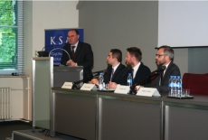 Wicedyrektor Krajowej Szkoły Administracji Publicznej Marek Haliniak przemawia do mikrofonu stojąc przy mównicy. Za stołem siedzi trzech uczestników spotkania, wśród nich niemiecki sekretarz stanu Michael Roth.