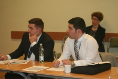 Dwóch uczestników wizyty studyjnej siedząc przy stole. Zwróceni w lewą stronę słuchają uważnie kogoś zza kadru. 