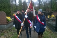 Poczet sztandarowy KSAP idzie pomiędzy grobami na cmentarzu.