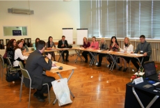 Widok sali i uczestników siedzących w ławkach ustawionych w kształt podkowy.