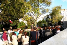 Słuchacze stoją przy pomniku.