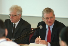 Bogusław Wind mówi do mikrofonu obok niego siedzi Jacek Czaputowicz