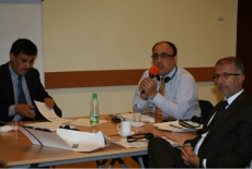 Trzech uczestników  szkolenia siedzi w ławkach, jeden z nich mówi do mikrofonu.