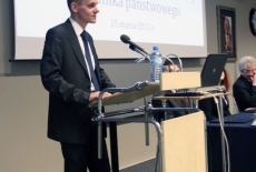 Pan Paweł Banaś stoi  przy mównicy i przemawia