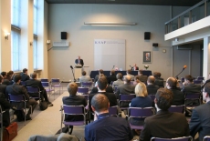 Widok ztyłu na siedzacych na Auli gości, Daniel Castello toi przy mównicy i przemawia