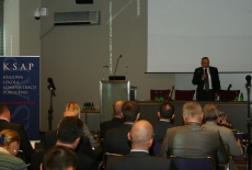 Przy stole prezydialnym stoi Pan i Mówi przez mikrofon do zebranych gości