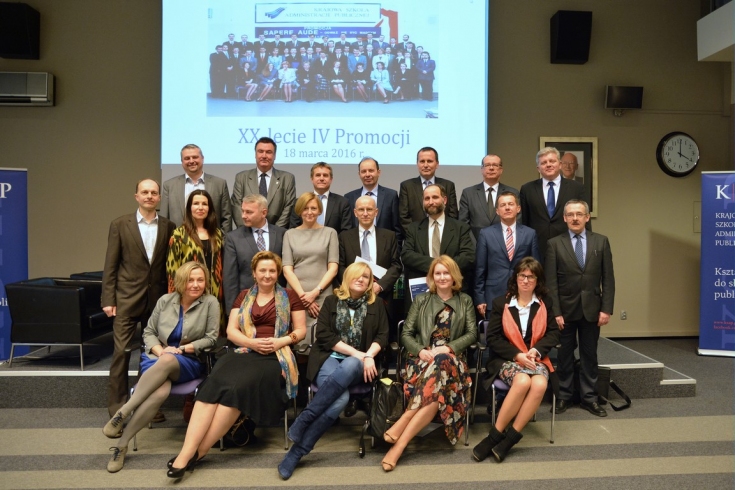 Zdjęcie grupowe absolwentów Promocji Sapere Aude. W tle wyświetlone archiwalne grupowe zdjęcie absolwentów z dnia rozdania dyplomów.