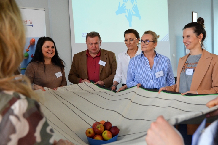 uczestnicy trzymają materiał, na którym stoi miska z jabłkami