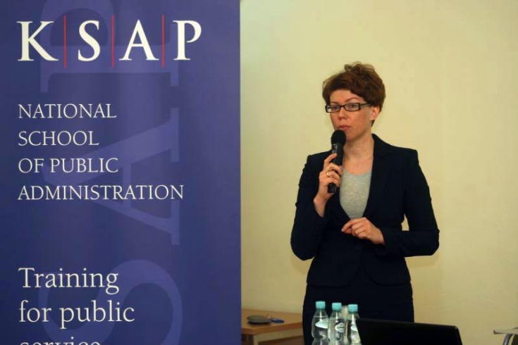 Katarzyna Woś mówi do miktofonu stojąc pod rollup KSAP.